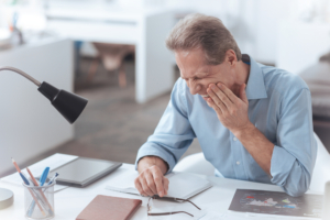 older man at desk wincing due to tooth pain