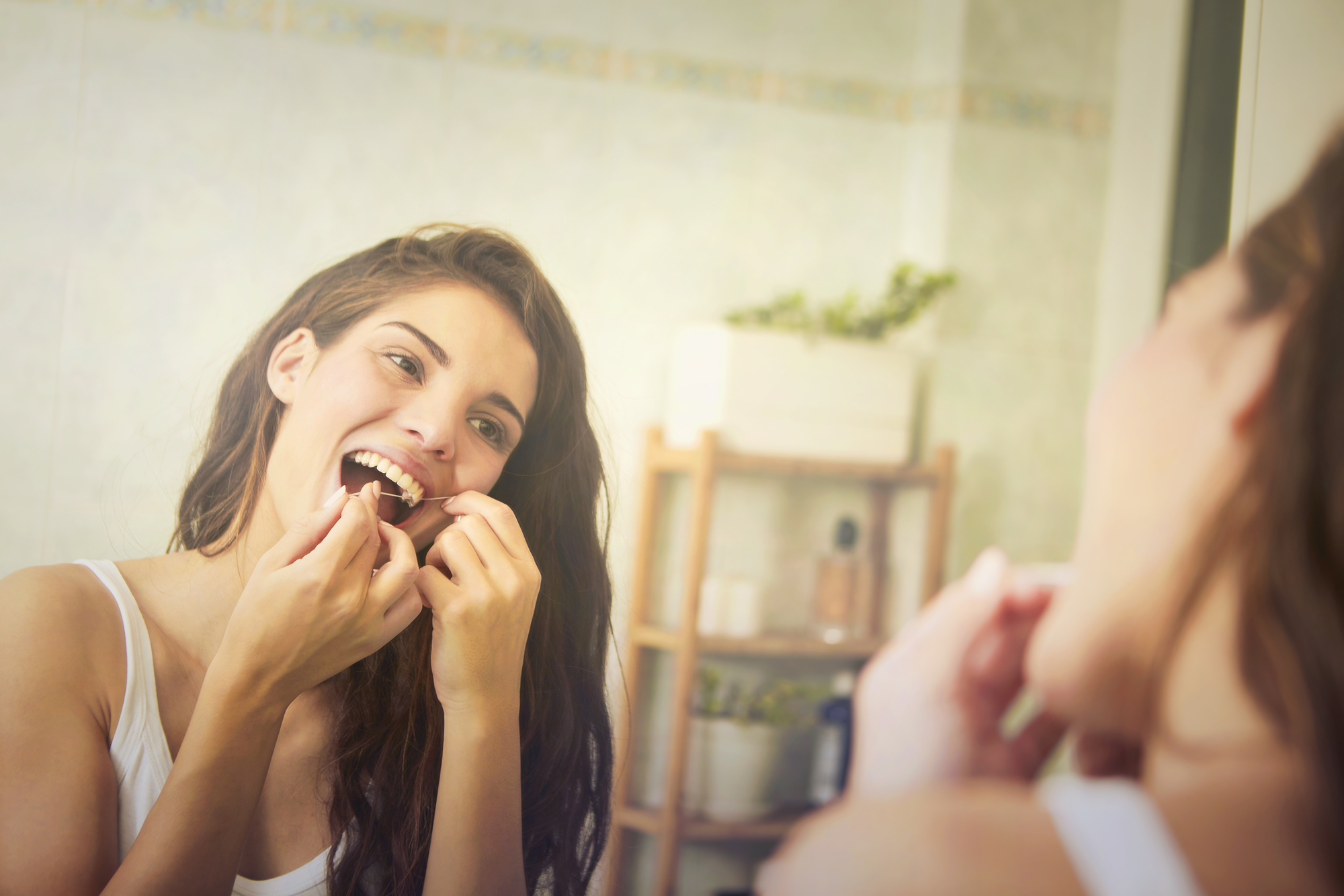 woman flossing teeth in mirror