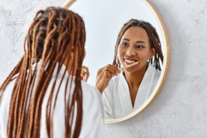 African American woman brushing teeth, looking in mirror, wearing a white robe