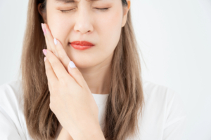 young woman experiencing dental pain, wincing, holding the side of her face