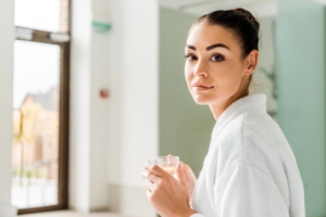 young woman in bathrobe holding cup of tea and looking at camera