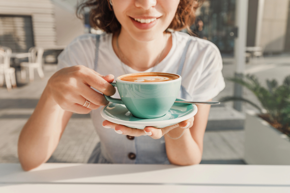 a happy woman drinks a fragrant fresh cappuccino coffee in an outdoor cafe