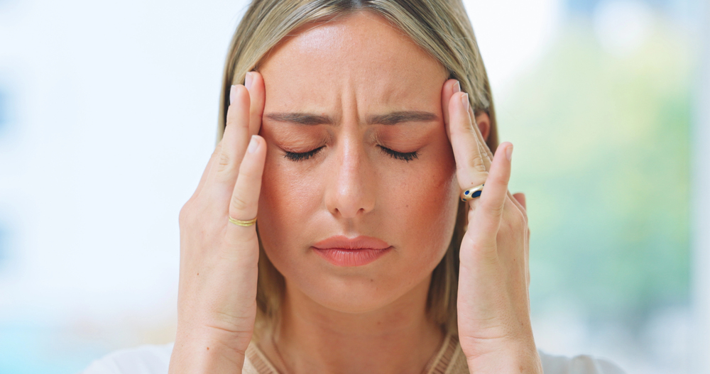 woman with a headache touching her temples and wincing