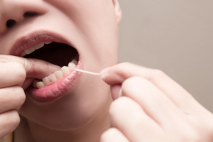 Asian woman using dental floss to remove food and dental plaque from between teeth in areas a toothbrush is unable to reach
