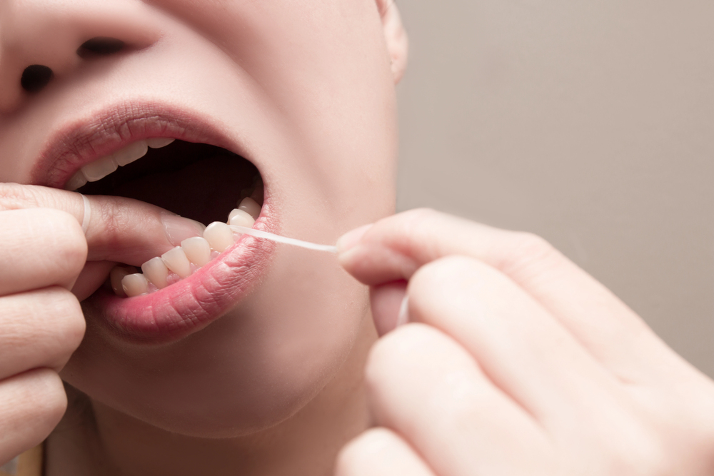 Asian woman using dental floss to remove food and dental plaque from between teeth in areas a toothbrush is unable to reach