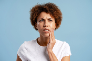 woman with dental crown pain wearing white shirt on blue background