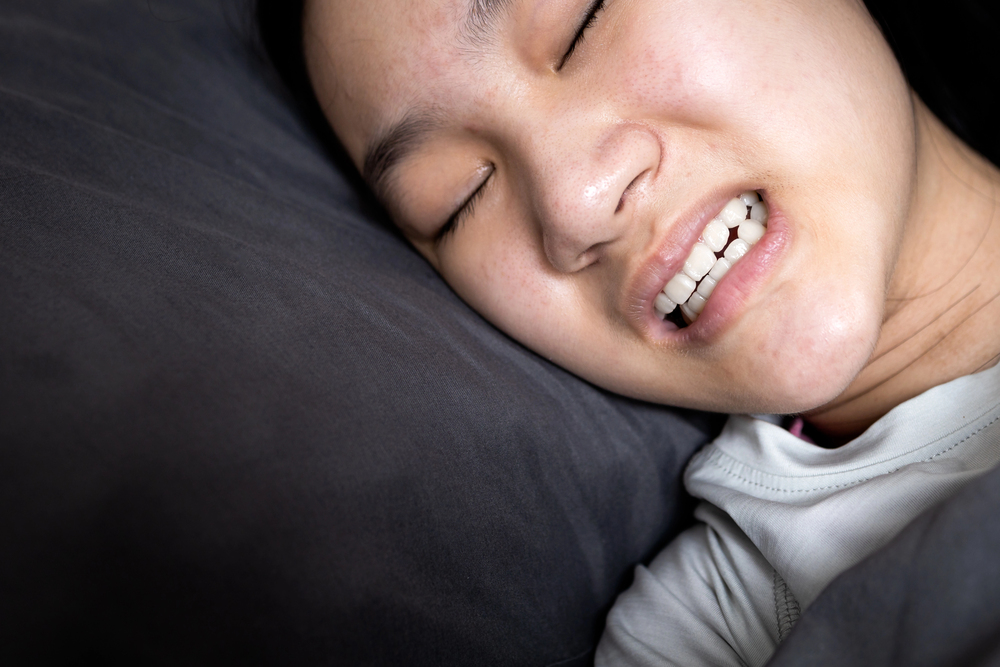 Asian child girl suffering from bruxism while lying in bed at night,female grinding of the teeth during sleep,teeth clenching,sleep disorders,oral health problems,dental care medical,bruxism concept